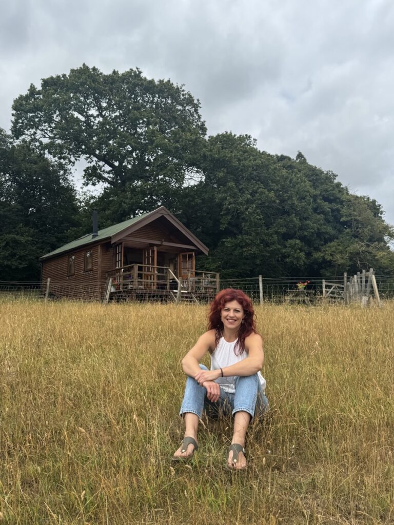 Chloe seated in a meadow with a wooden cabin behind her